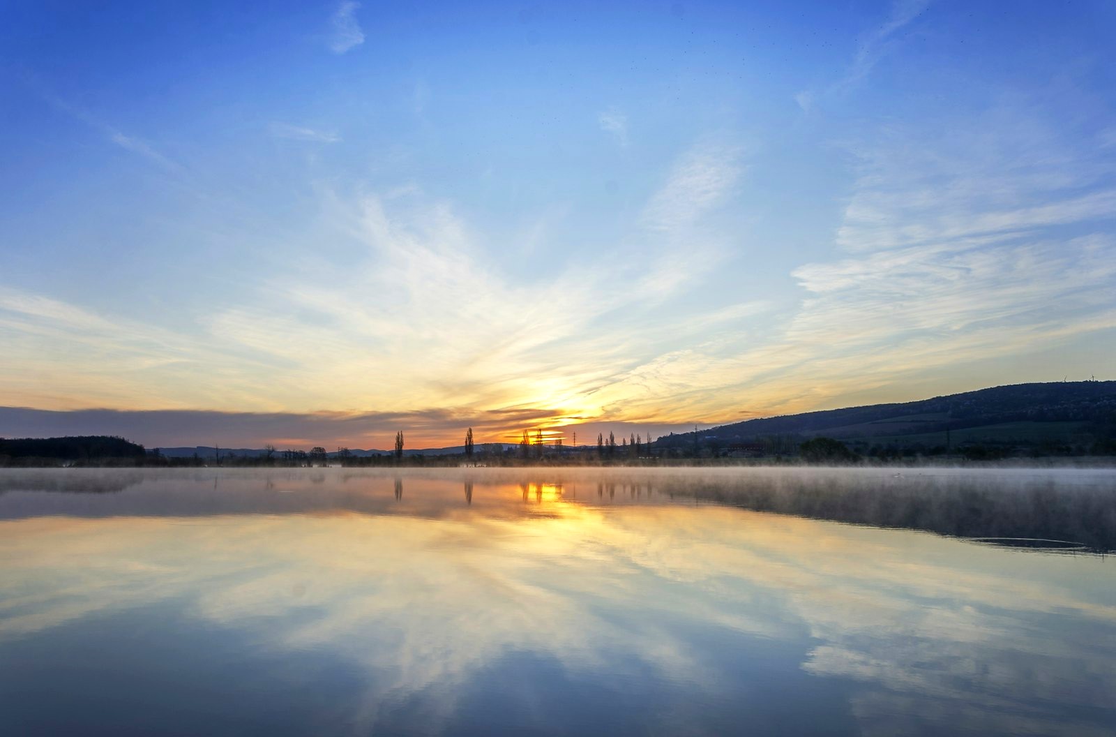 Sonnenaufgang über einem stillen See mit Spiegelung